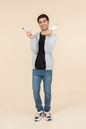 Laughing young caucasian man holding two smartphones