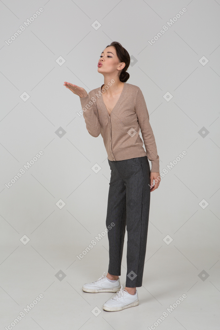 Vista de tres cuartos de una joven en suéter y pantalones enviando un beso al aire