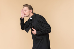 Catholic priest holding hand close to an ear and listening carefully