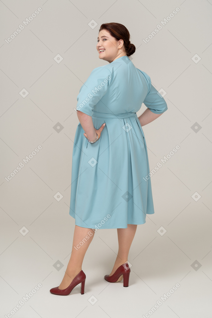 腰に手を置いて立っている青いドレスの幸せな女性の側面図