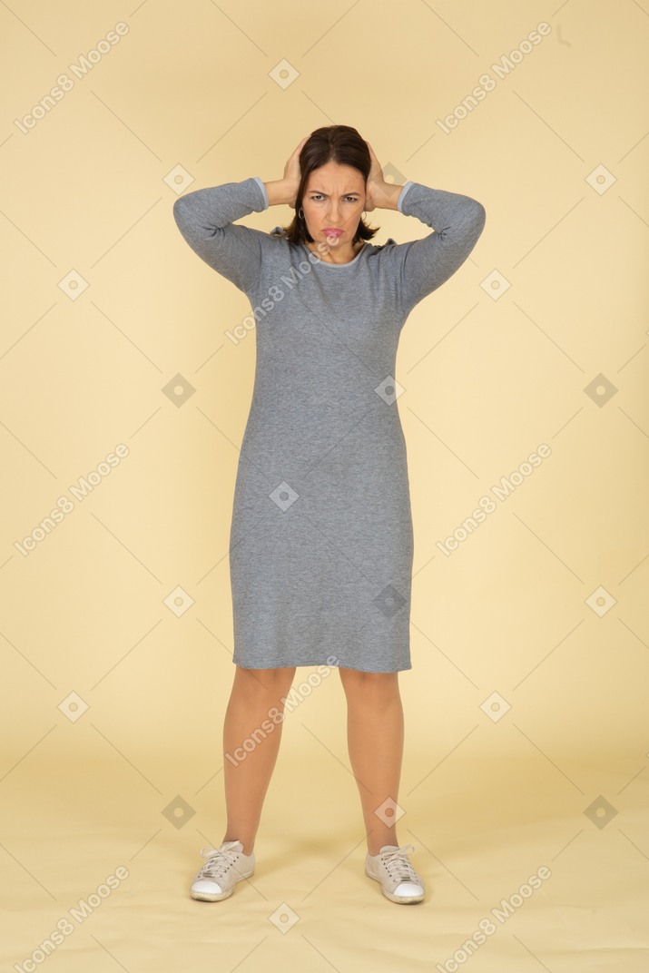 손으로 귀를 막는 회색 드레스를 입은 여성의 전면 모습