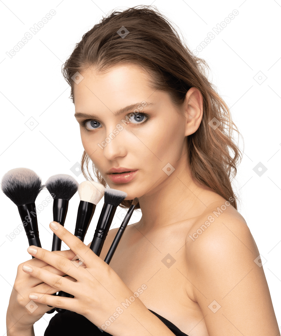 Vue de trois quarts d'une jeune femme sensuelle tenant des pinceaux de maquillage