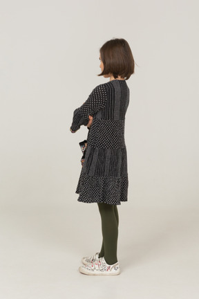 Vista posteriore di tre quarti di una bambina offesa in abito che incrocia le braccia