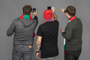 Vue arrière de trois fans de football masculins prenant des photos de téléphone