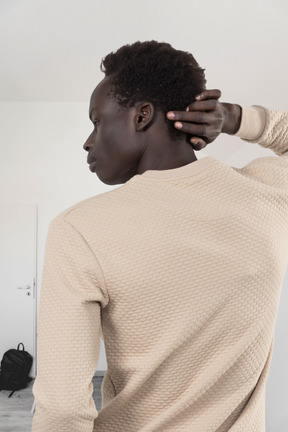 A black man in a tan sweater is standing in an empty room