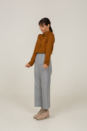 Vista di tre quarti di una giovane donna asiatica che fa smorfie in calzoni e camicetta che stringe i pugni