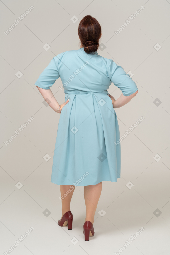 Vista trasera, de, un, mujer, en, vestido azul, posar, con, manos caderas