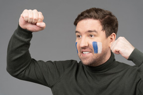 Three-quarter view of a male football fan with blue & white face art clenching fist