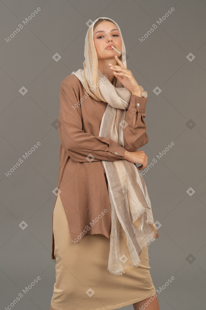 Woman in headscarf and beige clothes smoking a cigarette