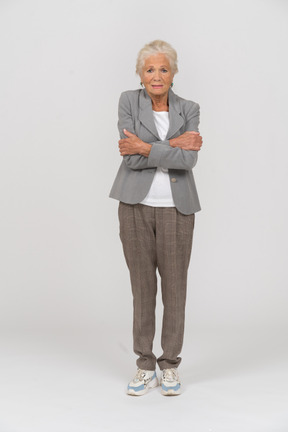 Vista frontal de una anciana en traje de pie con los brazos cruzados.