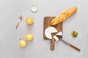 Tábua de cortar com alguma baguete e queijo, algumas pêras e mel