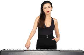 Vista frontal de uma jovem de vestido preto pressionando a tecla de um piano