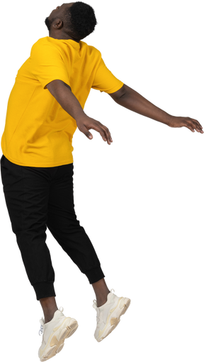 Three-quarter back view of a jumping young dark-skinned man in yellow t-shirt outspreading hands