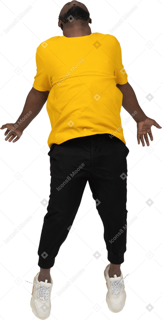 Vista frontal de um jovem de pele escura pulando em uma camiseta amarela estendendo as mãos