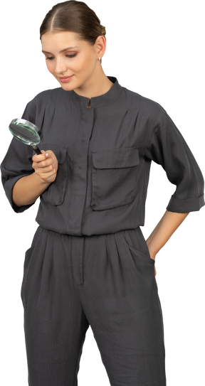 Front view of young woman in a jumpsuit holding a magnifying glass