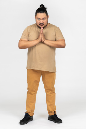 Serious asian man making praying gesture