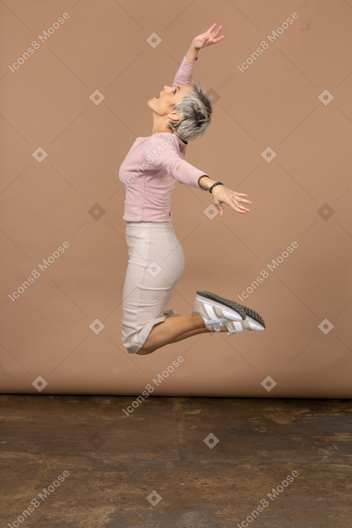 Vista laterale di una donna felice in abiti casual che salta con le braccia tese