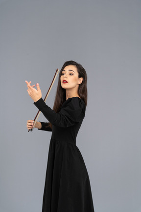 Vue de trois quarts d'une jeune femme en robe noire faisant l'impression de jouer du violon