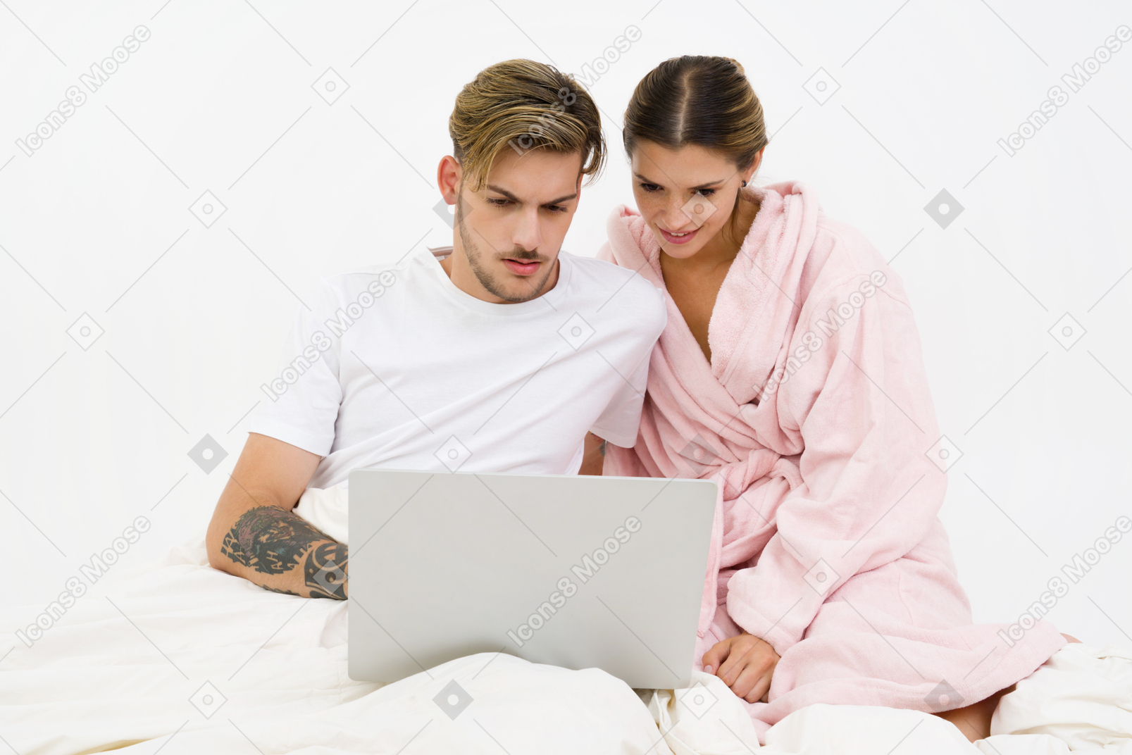 Couple assis dans son lit et travaillant sur un ordinateur portable