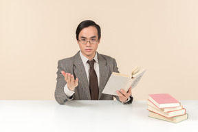 An asian teacher in a checkered suit, a tie and a book in his hand, working with the class