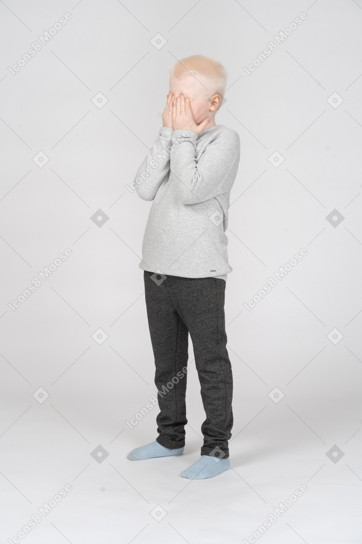Little boy standing and covering his face with his arms