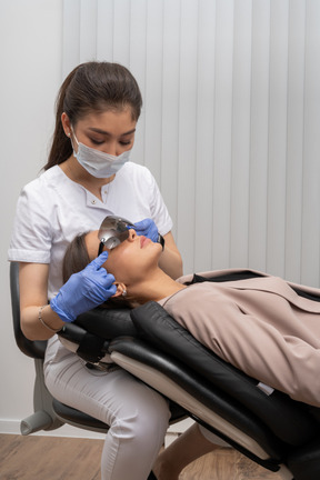 Female dentist in mask and latex gloves putting glasses on her patient