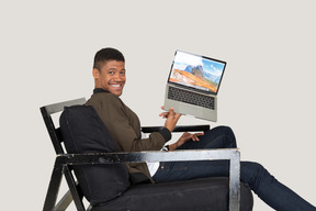 Side view of young man sitting on a sofa and holding a laptop