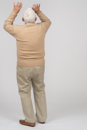 Rückansicht eines alten mannes in freizeitkleidung, der mit erhobenen händen steht