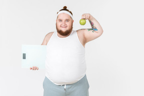 Big guy in sportswear holding scales and apple