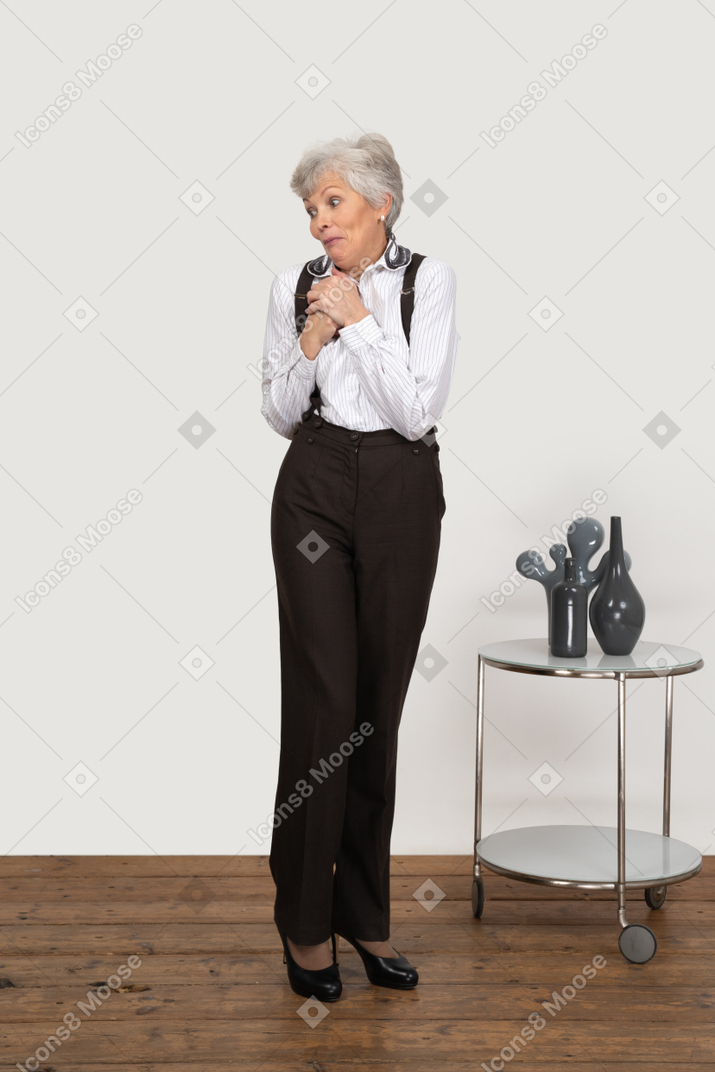 Front view of an old surprised funny lady in office clothing holding hands together