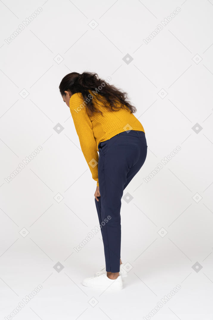 Rear view of a girl in casual clothes bending down and touching her hurting knee