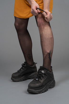 Foto recortada de uma pessoa em vestido laranja rasgando meia-calça