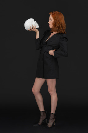 A three-quarter side view of the beautiful young girl holding a skull on the dark background