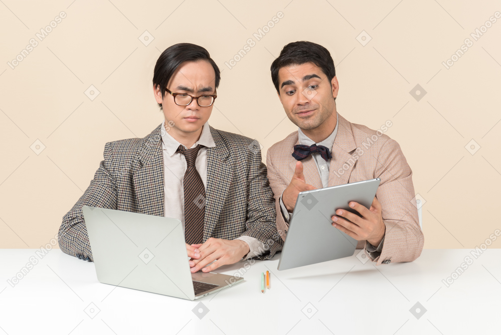 Two young nerds sitting at the table and using gadgets