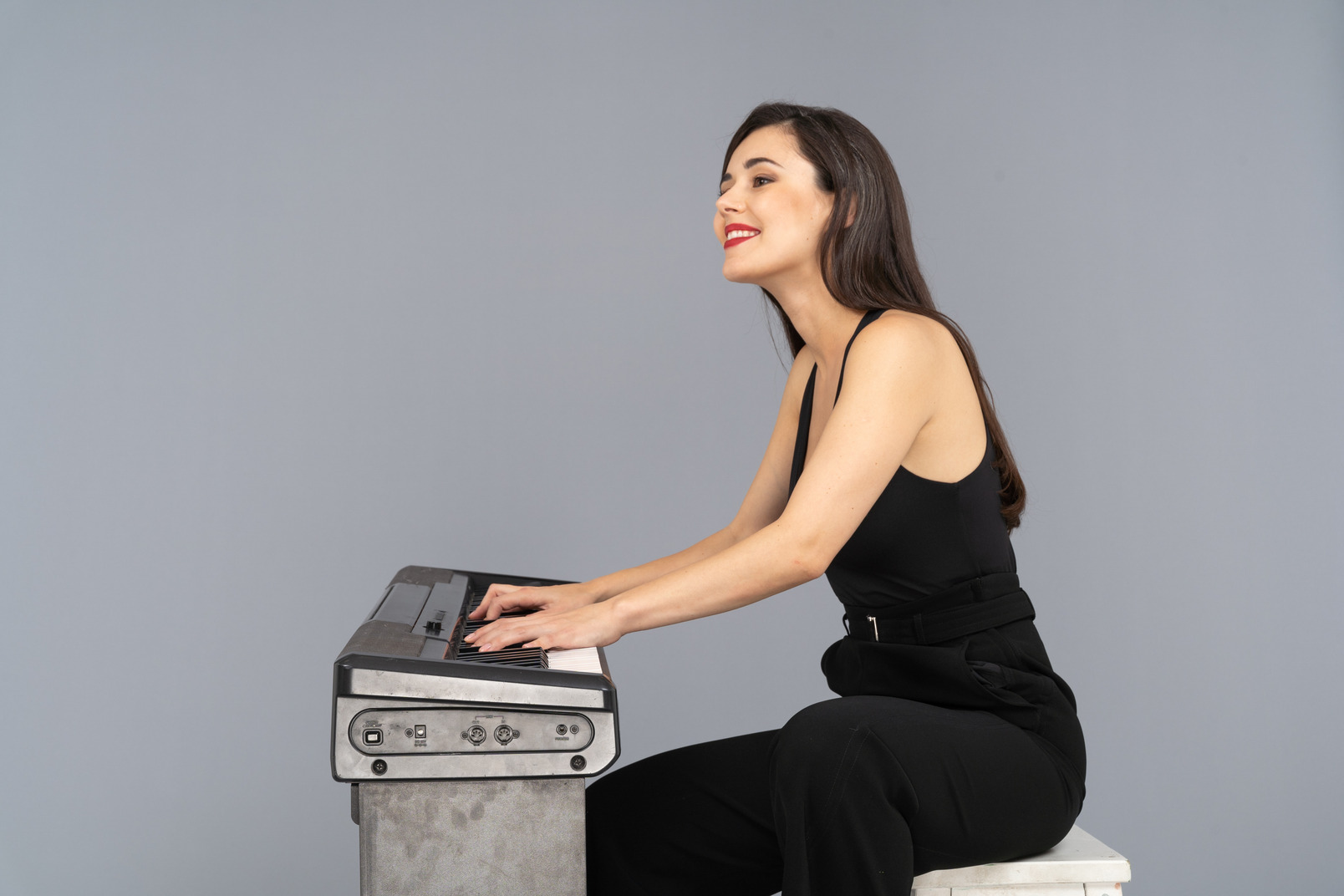 Side view of a smiling sitting young lady in black suit playing the piano