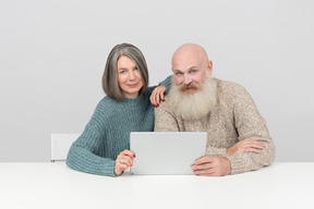 Casal mais velho sentado à mesa e olhando para tablet