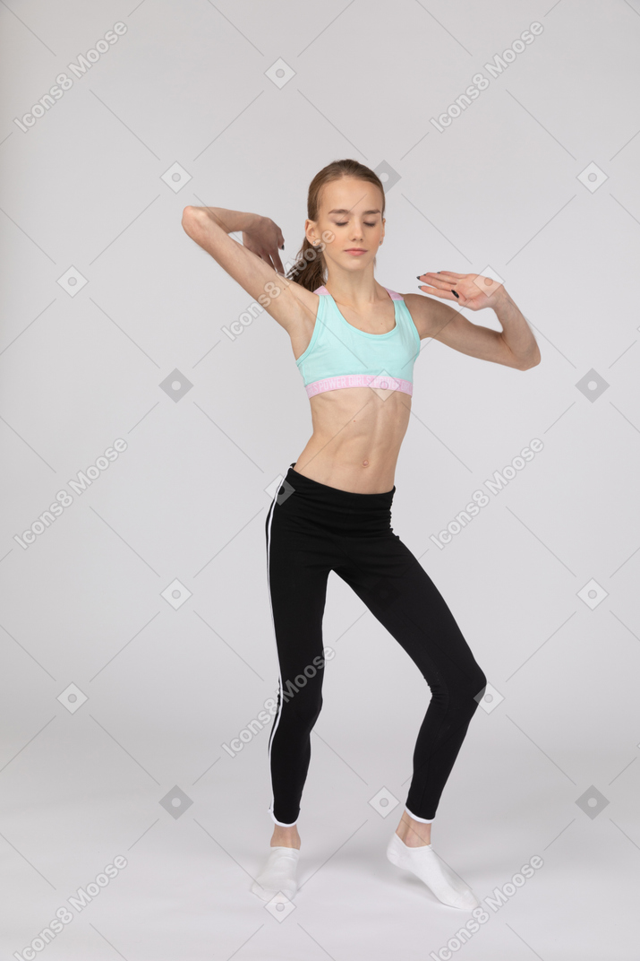 Vista de tres cuartos de una jovencita en ropa deportiva levantando ambas manos mientras baila