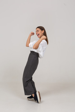 Three-quarter view of a happy young lady in office clothing raising hands