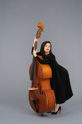 Vista di tre quarti di una giovane musicista in abito nero che tiene il suo contrabbasso proteso in avanti