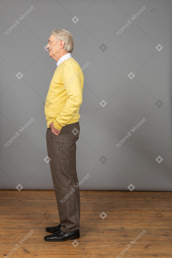Side view of a displeased old man wearing yellow pullover and putting hand in pocket