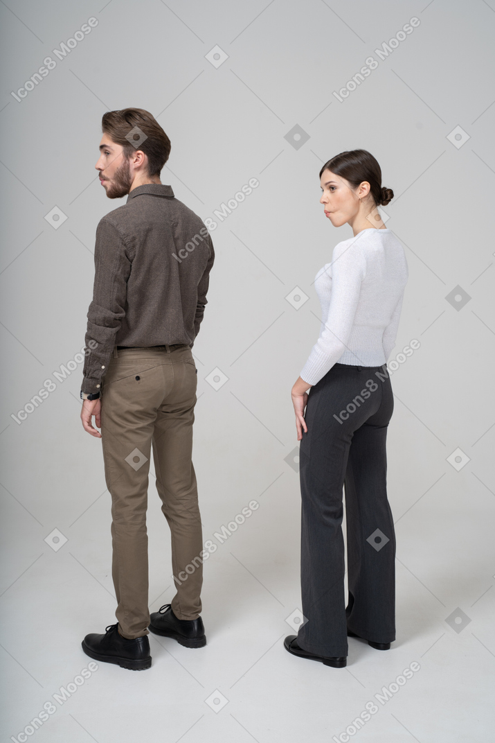 Vista posterior de tres cuartos de una pareja joven en ropa de oficina metiendo las mejillas