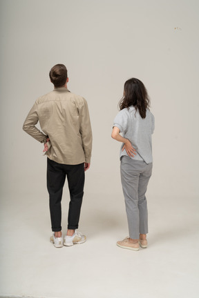 Young man and woman standing with hand on side and looking away