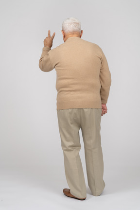 Vista trasera de un anciano con ropa informal que muestra el signo v
