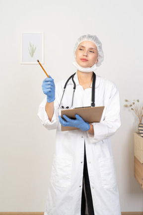 Vista frontal de una joven doctora sosteniendo una tableta y apuntando a un lado