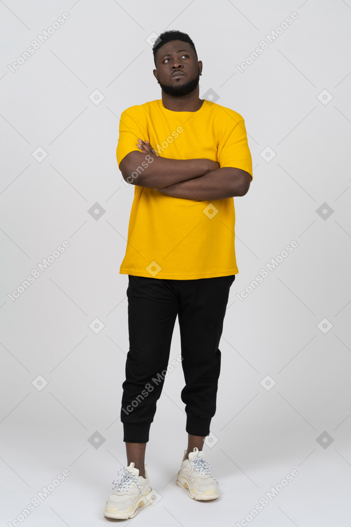 Vorderansicht eines verdächtigen jungen dunkelhäutigen mannes in gelbem t-shirt, das die arme verschränkt