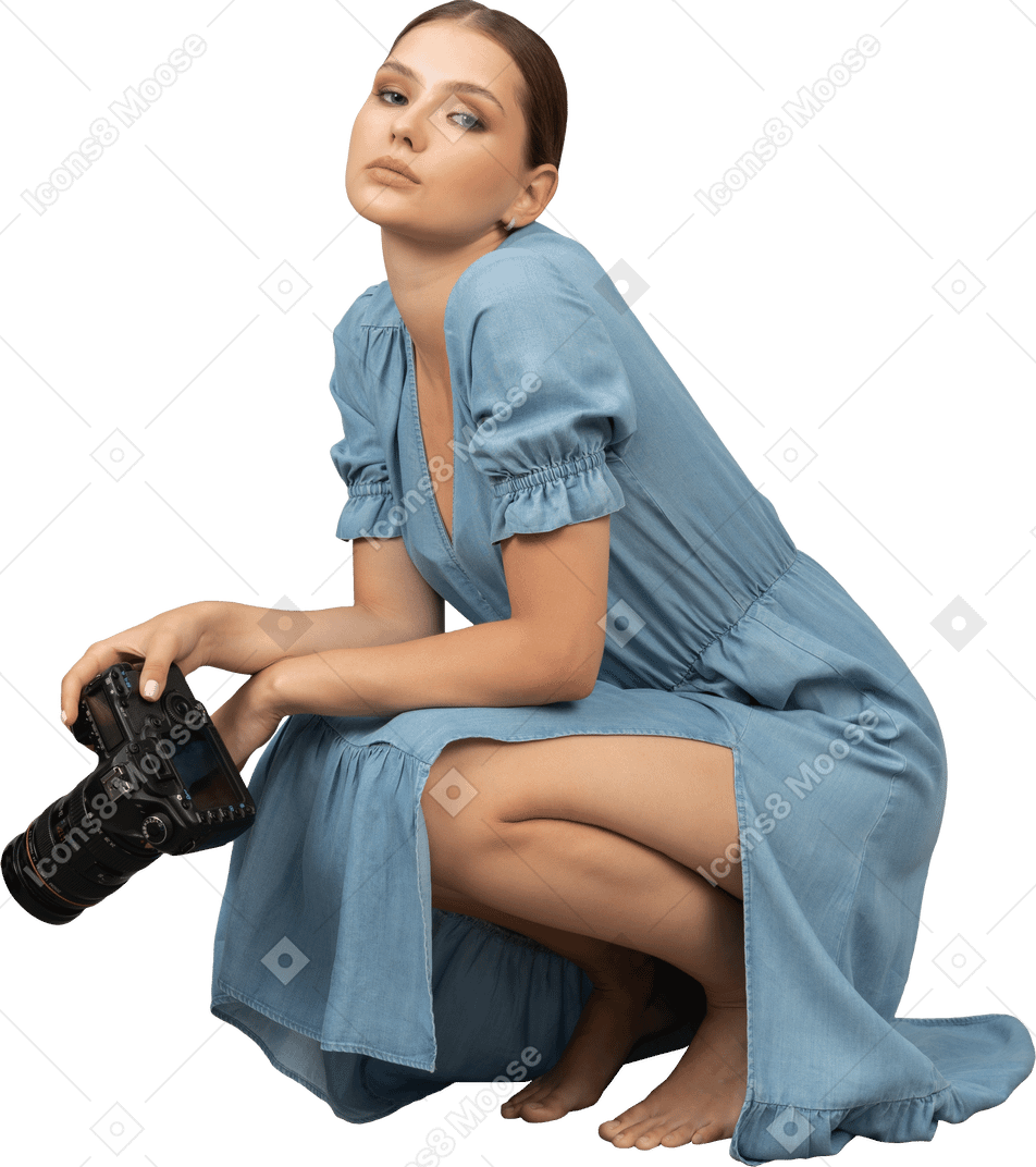 Вид сбоку молодой женщины в синем платье, сидящей на полу с камерой