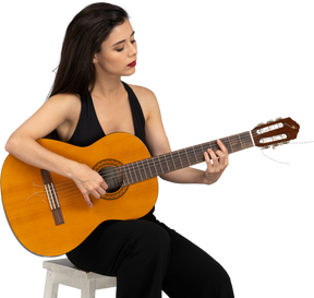 Вид спереди сидящей молодой леди в черном костюме, играющей на гитаре