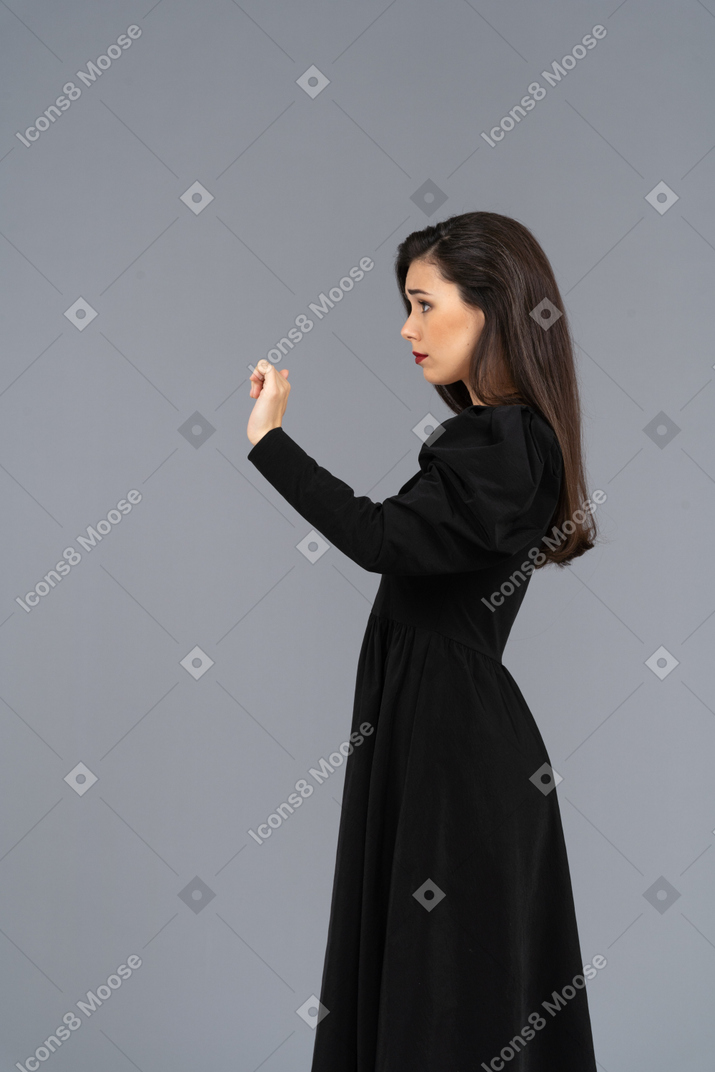 그녀의 손을 올리는 검은 드레스에 젊은 아가씨의 측면보기