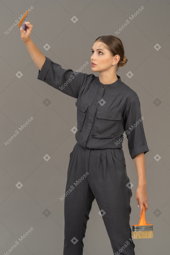 페인트 브러시와 함께 포즈를 취하는 회색 작업복을 입은 여자