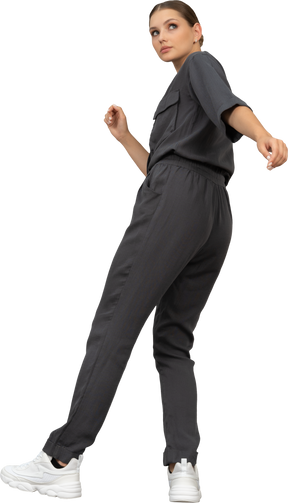Three-quarter back view of a young woman in a jumpsuit outstretching her arm